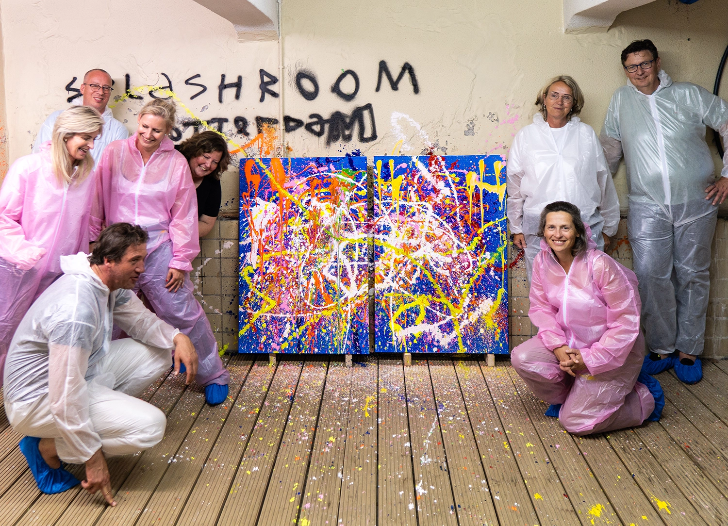 Team in roze en witte overalls naast twee Splash Painting-doeken na een teamdag bij Dutch Art Room in Rotterdam