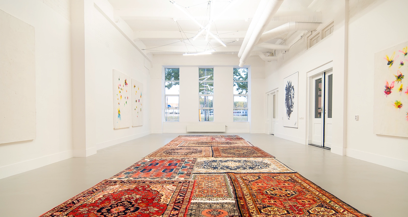 Witte galeriezaal met hoge plafonds, grote ramen, Perzische tapijten en werk van Simonian aan de muren bij Dutch Art Room in Rotterdam
